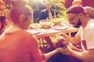leisure, summer holidays, eating, people and food concept - happy friends with french bulldog dog having dinner at garden party